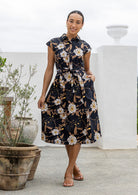Woman wearing a shirt style cotton midi length dress with buttoned bodice, pockets, collar and cap sleeves