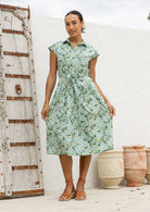 Woman wearing a shirt style cotton midi length dress with buttoned bodice, pockets, collar and cap sleeves