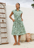 Model posing in a sage green based floral print shirt style 100% cotton dress with cap sleeves and detachable waist tie