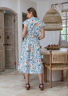 Model stands backwards near wearing a mid length, shirt style floral print cotton dress with white based floral print