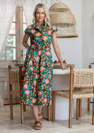 Model stands with wearing a midi length floral printed shirt style cotton dress with cap sleeves, buttoned bodice. 