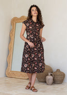 Woman wearing a shirt style cotton midi length dress with buttoned bodice, pockets, collar and cap sleeves