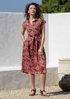 Woman wearing a midi length Japanese style floral print cotton dress with buttoned bodice, standing against a white wall and decorative vases