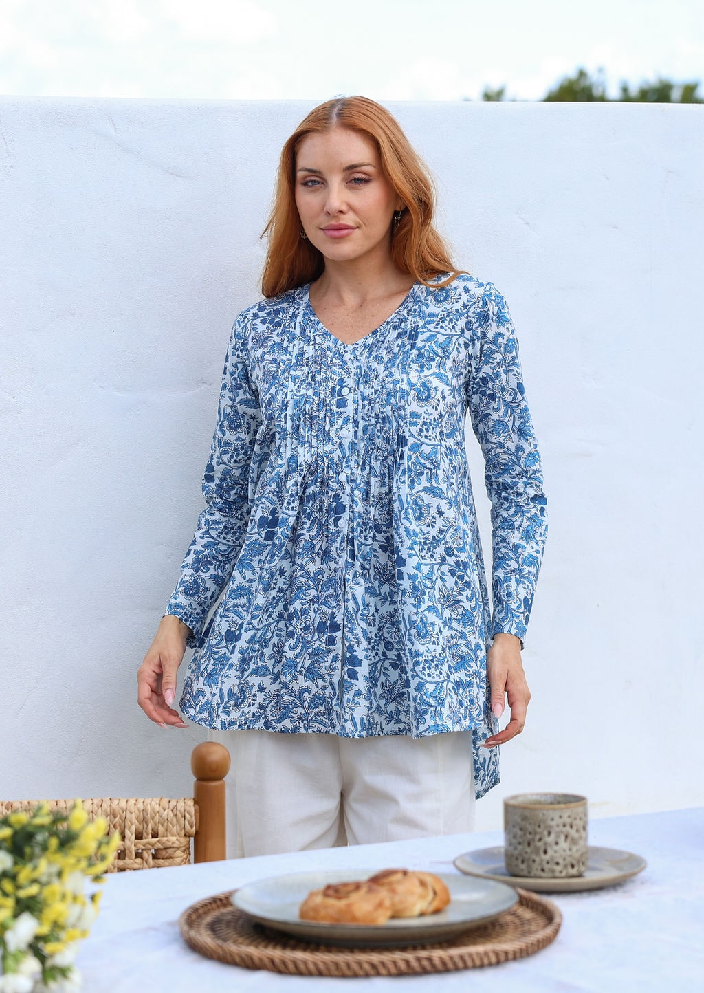 Woman wearing a cotton white based blue floral print tunic top with long sleeves and pintuck front. 