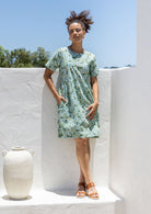 Woman wearing a above knee length floral cotton dress with short sleeves, pockets and round neckline 
