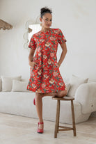 Woman poses with both hands in pockets of a 100% cotton relaxed fit dress with round neckline and short sleeves.
