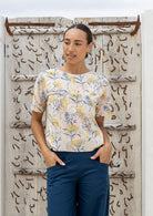 Woman wearing a 100 percent cotton, neutral based floral loose cut top with high round neckline and short sleeves