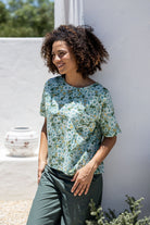 Woman wearing a 100 percent cotton, sage green based floral loose cut top with high round neckline and short sleeves