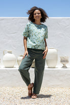 Woman in sage green based floral cotton top with short sleeves, round neckline and plain green pants.