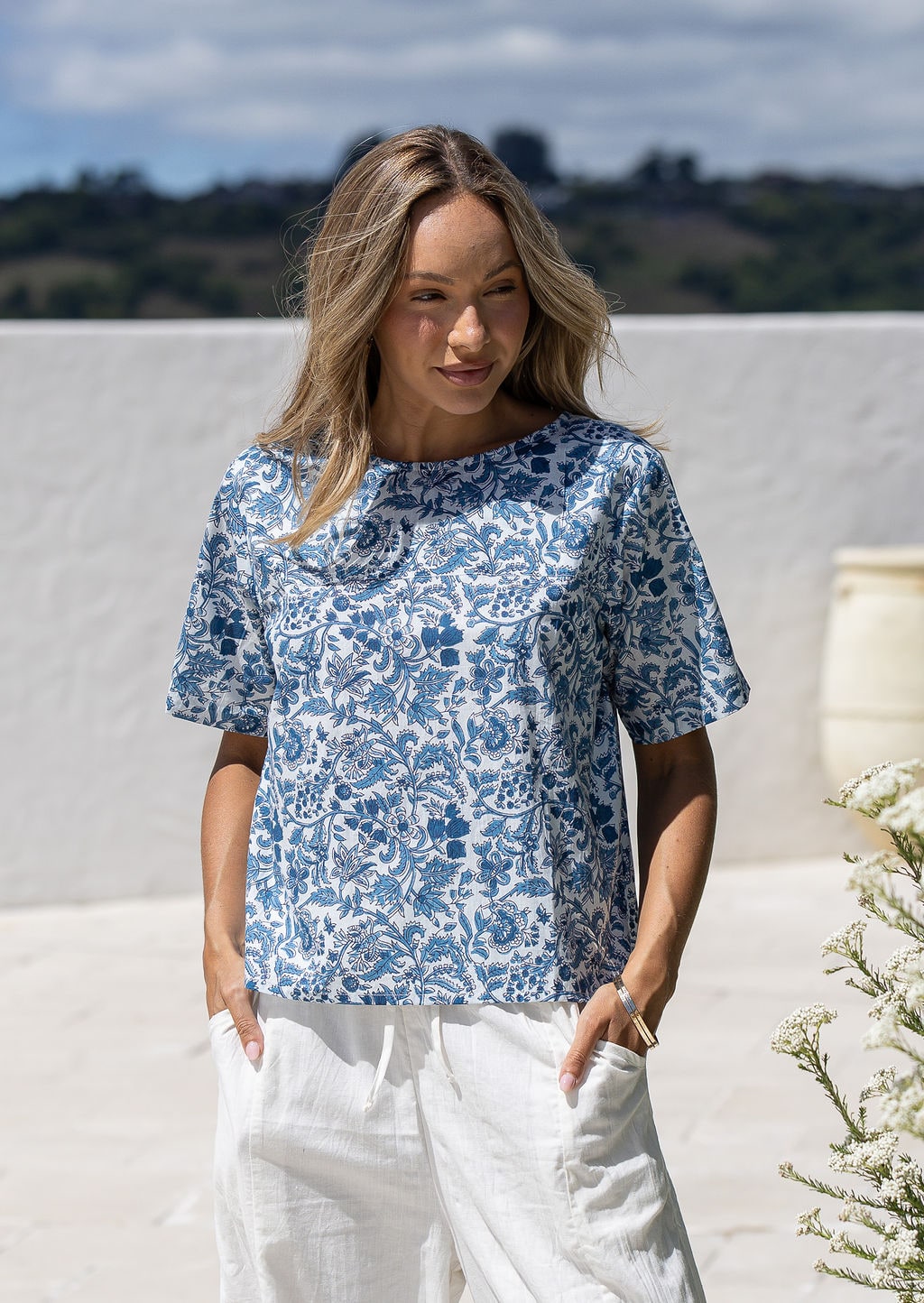Woman wearing a white based blue floral printed relaxed fit cotton top with short sleeves and high neckline
