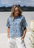 Woman wearing a white based blue floral printed relaxed fit cotton top with short sleeves and high neckline
