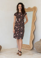 Model wears a simple knee length cotton dress with round neckline, short cap sleeves, pockets and a slight A-line skirt.