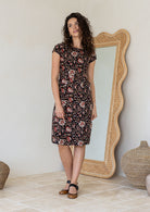 Model standing in a 100% cotton dress in Indian traditional floral print cotton dress with with rust, tan and sand tones on a black base.