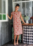 Woman wearing 100% cotton cream based floral sundress with round neckline, cap sleeves, A line skirt and pockets