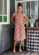 Woman wears a 100% cotton, knee-length A-line floral dress with both hands in pockets. 