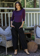 Woman standing in front of a porch wearing black cotton corduroy pants with hands in pockets