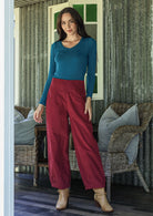 Woman wearing a blue top and red pants standing in a rustic indoor setting.