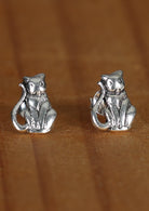 Close-up image of Happy Cat silver cat-shaped stud earrings sitting on a wood surface.