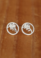 A pair of sterling silver Alp stud earrings with intricate mountain cutout details, displayed against a wooden background.