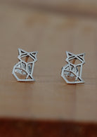 A pair of silver geometric fox stud earrings placed on a wooden surface.