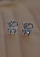 A pair of sterling silver earrings in the shape of kittens, displayed against a wooden background.
