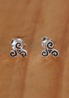 A pair of sterling silver stud earrings with a triskele design, displayed on a wooden surface 