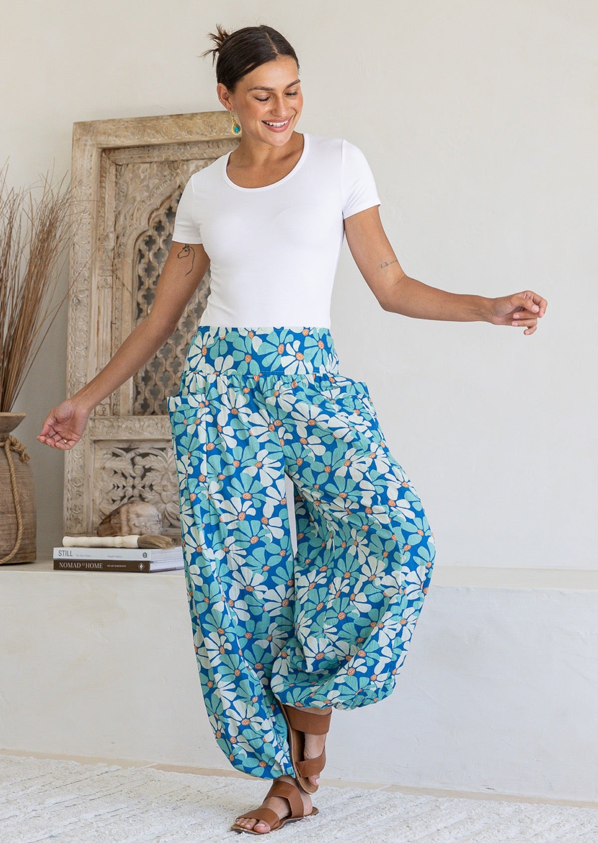 Woman poses in cotton harem pants in blue and aqua daisy print, paired with a white stretch rayon top