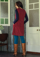 Woman stands backwards wearing a red dress and blue leggings standing in a room with patterned curtains and a white door.