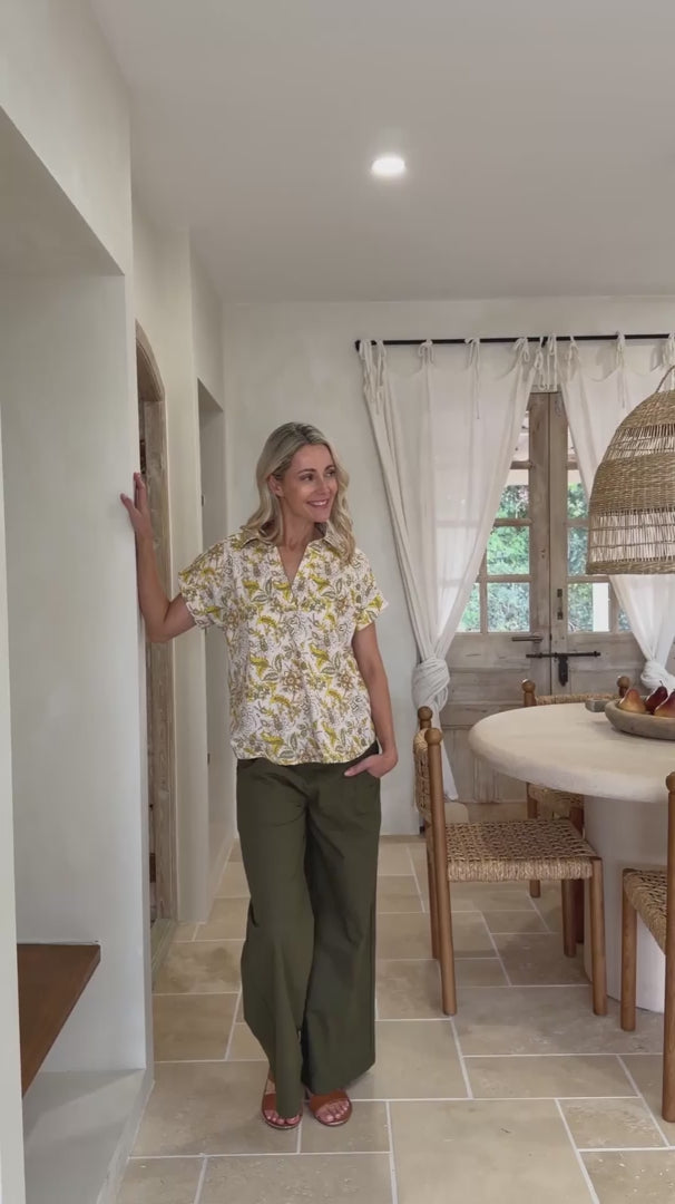 Video of a woman poses in relaxed fit cotton short sleeve top with rolled cuffs sleeves, collar and V neckline.