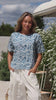 Video of a woman wearing a white based blue floral printed relaxed fit cotton top with short sleeves and high neckline