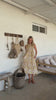 Video of a model wears 100% cotton sleeveless midi dress with high round neckline, tiered design and pockets in cream based floral print