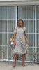 Video of a woman wearing a white based cotton floral short sleeve dress with round neckline and hand in pockets