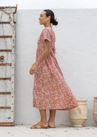 Woman stands sideways wearing a 100% cotton dress with short sleeves, pockets, and a drawstring tie at the back.