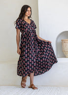 Woman wearing a cotton Black floral maxi dress with short sleeves and V-neck skirt held out to show flare.