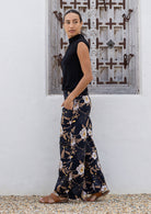 Model poses in black floral cotton pants with side zipper, pockets and wide leg fit
