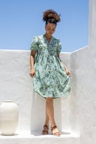 Woman wearing sage green based floral print 100% cotton dress with, relaxed fit, empire waistline and elasticated elbow length sleeves