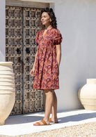 Side view of woman wearing a knee length relaxed fit 100% cotton dress in warm toned standing in an outdoor setting