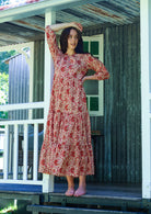 Woman poses floral cotton maxi dress with buttoned bodice, 3/4 sleeves and flowy three tiered maxi skirt