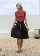 Woman standing outdoors wears 100% cotton tailored knee length skirt with button up front, box pleats and pockets