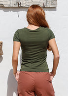 Woman standing backwards wearing a 100% rayon fitted scoop round neck short sleeve double stitch hem soft stretch in olive green. 