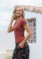 Woman wearing a terracotta shirt and floral pants standing outdoors with a house in the background