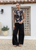 Woman holding the bottom hem of sleeveless black based floral top paired with black pants