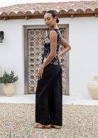 Woman standing side on wearing a black sleeveless top with floral patterns against a wooden door.