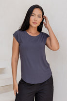 Woman wearing a 100% rayon grey shell t-shirt and black cotton pants against a white wall.