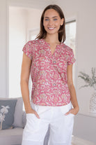 Woman wearing a 100% cotton warm pink based floral blouse and white pants.