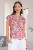 Woman wearing a 100% cotton warm pink based floral blouse and white pants.