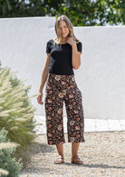 Woman wearing a black basic rayon top and black based floral print wide leg 3/4 cotton pants with side zipper and pockets