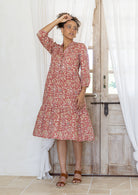Woman flaunting cotton tiered dress in rose pink floral print, with 3/4 sleeves, buttoned bodice and V-necklin