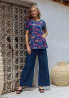 Woman standing with hand in top's pocket, wearing a lightweight 100% cotton blue floral print top with dark blue cotton pants
