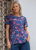 Woman wearing a blue floral print top with short sleeves, an empire waistline and deep pockets, standing against a wooden door
